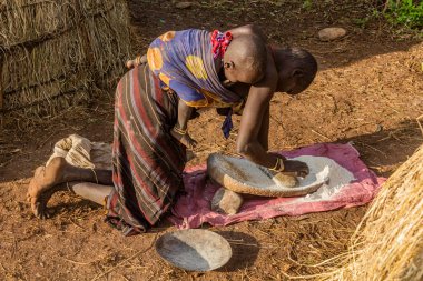 OMO VALLEY, ETHIOPIA - 6 Şubat 2020: Mursi kabilesi kızı Etiyopya 'daki köyünde tahıl öğütüyor