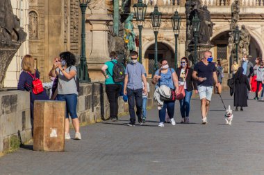 PRAG, CZECHIA - 27 Nisan 2020: Maskeli adamlar Çek Cumhuriyeti 'ndeki COVID-19 karantinası sırasında Prag' daki Charles Köprüsü 'nden geçiyorlar.