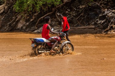 OMO VALLEY, ETHIOPIA - 4 Şubat 2020: Etiyopya, Etiyopya 'daki Kizo Nehri' nin taşmış sularından geçen motosikletli çocuk
