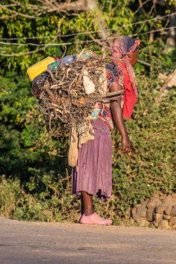KONSO, ETHIOPIA - 7 Şubat 2020: Konso, Etiyopya yakınlarında bir sürü tahta ve plastik kap taşıyan kadın