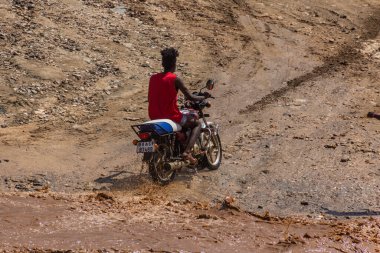 OMO VALLEY, ETHIOPIA - 4 Şubat 2020: Etiyopya, Etiyopya 'daki Kizo Nehri' nin taşmış sularından geçen motosikletli çocuk