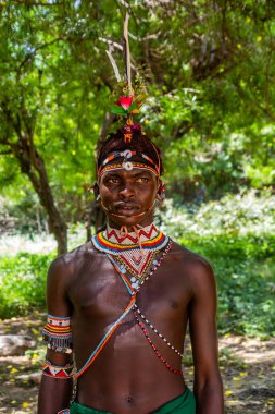 GÜNEY HORR, KENYA - 12 Şubat 2020: Samburu kabilesi delikanlısı sünnet töreninden sonra devekuşu tüylerinden yapılmış renkli bir başlık takıyor. Kenya 'nın Güney Horr köyünde çekildi.