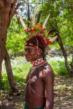 GÜNEY HORR, KENYA - 12 Şubat 2020: Samburu kabilesi delikanlısı sünnet töreninden sonra devekuşu tüylerinden yapılmış renkli bir başlık takıyor. Kenya 'nın Güney Horr köyünde çekildi.