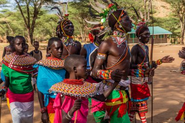 GÜNEY HORR, KENYA - 12 Şubat 2020: Samburu kabilesinden genç erkekler ve kadınlar malecircumsion seremonisinden sonra devekuşu tüylerinden yapılmış renkli başlıklar takarak dans ediyorlar.