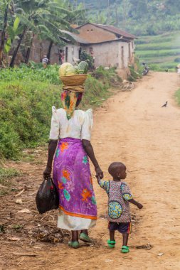 BUHUTU, UGANDA - 19 Mart 2020: Uganda 'nın Bunyonyi Gölü yakınlarındaki Buhutu kasabasında kafasında sebze sepeti taşıyan yerel bir kadın