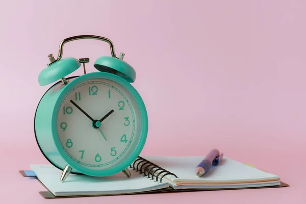 Ένα Ξυπνητήρι Καμπάνα Ένα Σημειωματάριο Και Ένα Στυλό Ροζ Φόντο — Φωτογραφία Αρχείου