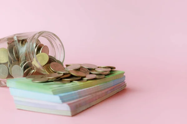 stock image A glass jar of coins with banknotes on pink background for the concept of business and finance.