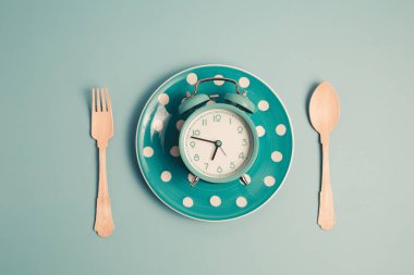 Yemek, zaman yönetimi, kilo verme ve zamanında yemek yeme kavramına karşı mavi arka plan üzerine kurulmuş boş bir tabak ve çatal bıçak seti..