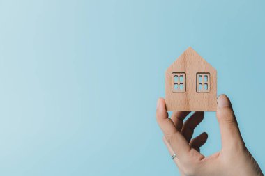 Ev ve konut kavramları için mavi arka planda ahşap bir ev modeli tutuyorum.