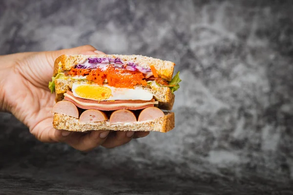 Hand Hält Ein Leckeres Sandwich Auf Dunklem Hintergrund Für Bäckerei — Stockfoto