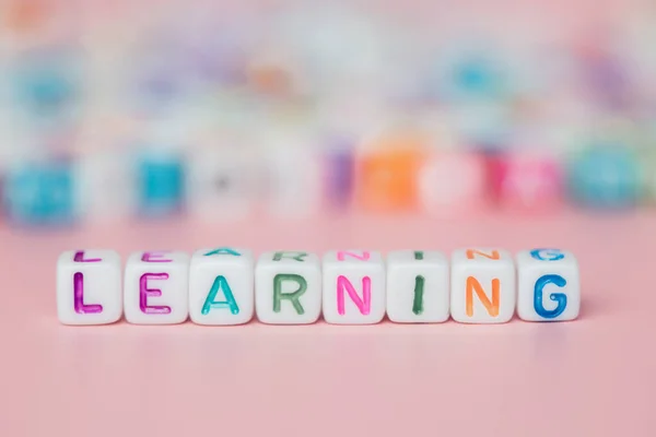 The word LEARNING from letter beads on pink background for education and studying concept, selective focus image