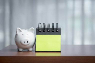 Piggy bank and notepad on a wooden table with copy space, embodying the concept of combining financial mindfulness with thoughtful planning and the potential for recording ideas or goals. clipart