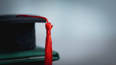 Mezuniyet şapkası diplomaya dayanıyor. Akademik başarının sembolü, eğitim başarısı, mezuniyet töreni, üniversite diploması ve öğrenci başarısı.