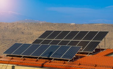 Güneş panellerinin fotoğrafı, kırmızı çatıdaki fotovoltaikler ve dağlar ve güneşli güzel bir gökyüzü. Alternatif elektrik kaynağı. Sürdürülebilir kaynaklar kavramı