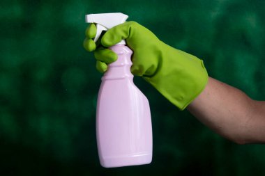 Yeşil arka planda ev hijyeni için kullanılan temizlik ürünlerinin paketini tutan koruyucu eldivenli bir el.