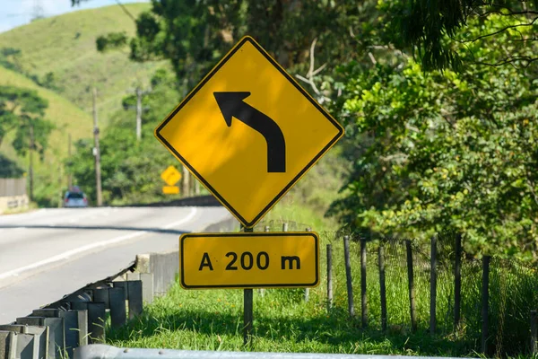 yellow road sign signaling a forward curve on a road in Brazil