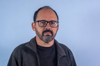 60 yaşında bir adam kameraya bakıyor.