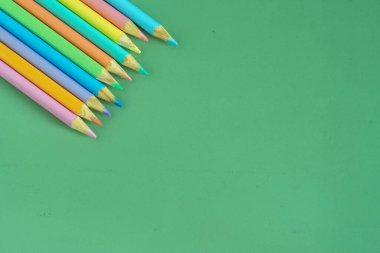 Pastel colored pencils, top view on green background, illustration concept, background and education and back to school