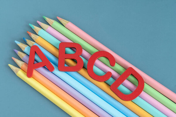 Вернуться к школьной концепции с разнообразными буквами и цветными карандашами в пастельных цветах на синем фоне