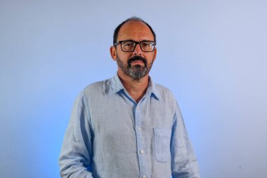 60 yaşında bir adam mavi arka planda kameraya bakıyor.