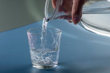 Detail of person filling glass of water. hydration concept in blue background