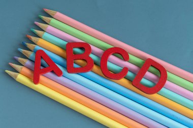 Back to school concept with assorted letters and colored pencils in pastel colors in blue background