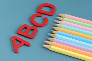 Back to school concept with assorted letters and colored pencils in pastel colors in blue background