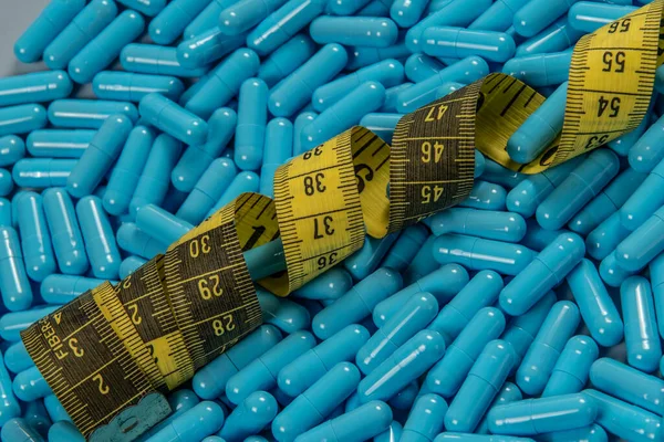 Weight loss blue gelatin pills and measuring tape symbolizing slimming