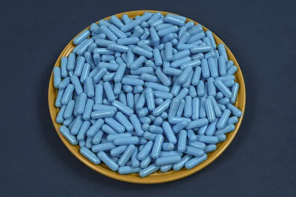 薬物過剰摂取を表す青い薬のカプセルでいっぱいの黄色いプレート トップビュー — ストック写真