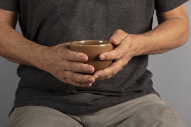Hands of an elderly man holding a mug with a hot drink. Cup of coffee or tea