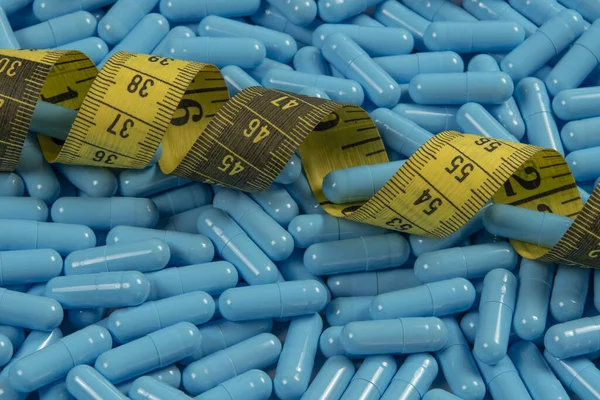 Weight loss blue gelatin pills and measuring tape symbolizing slimming