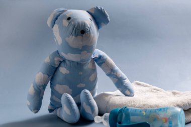 Havlu ve bebek şişesiyle bez bebek mavi tonda çocukluğu temsil ediyor.