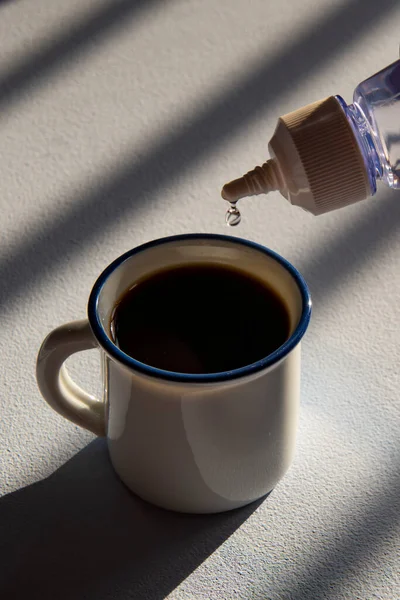 person sweetening coffee with liquid sweetener, scene showing cup and flask