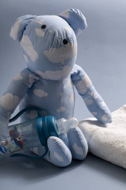 Havlu ve bebek şişesiyle bez bebek mavi tonda çocukluğu temsil ediyor.