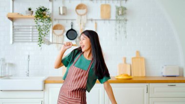 Asyalı genç bir kadın mutfak odasında dans ediyor. Hafta sonları boş zamanlarında mutlu ve rahatlatıcı bir kadın.