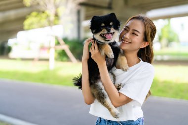 Happy young asian woman playing and sitting on road in the park with her dog. Pet lover concept clipart