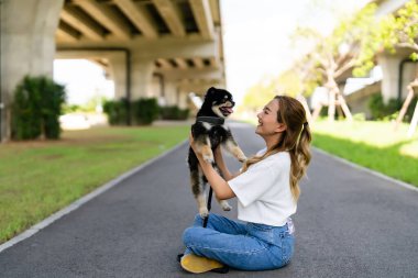Happy young asian woman playing and sitting on road in the park with her dog. Pet lover concept