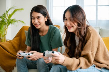 Two people beautiful young asian woman sitting on sofa and holding joystick remote control playing online video game in living room