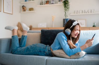 Mutlu Asyalı kadın evde dinleniyor. Kanepede oturan ve elinde cep telefonu tutan bir kadın gülümsemesi. Arkadaşı ile görüntülü konuşma yapan bir kız. Müzik dinliyordum.