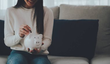 Asyalı kadın domuz kumbarasına para koyuyor. Para ve yatırım kavramını sakla