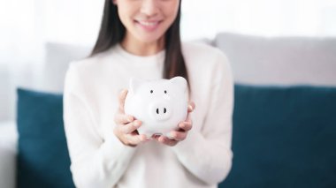 Genç Asyalı kadın beyaz domuz kumbarasını evde tutuyor. Para ve yatırım kavramını sakla