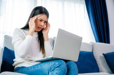 Ofis sendromu. Çok çalışan yorgun Asyalı kadın baş ağrısı çekiyor, bilgisayardan sonra görme sorunu yaşıyor. Evde yorgunluk çeken stresli genç bir kadın.