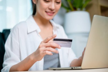 İş yerinde çalışan Asyalı genç bir kadın, internet üzerinden bilgisayar laptopunda banka kartıyla online bankacılık ödemeleri yapıyor. Kredi kartıyla internet üzerinden alışveriş yapmak