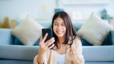 Happy young asian woman relax on comfortable couch at home texting messaging on smartphone, smiling girl use cellphone, chatting online message, shopping online from home