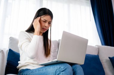 Ofis sendromu. Çok çalışan yorgun Asyalı kadın baş ağrısı çekiyor, bilgisayardan sonra görme sorunu yaşıyor. Evde yorgunluk çeken stresli genç bir kadın.