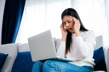 Ofis sendromu. Çok çalışan yorgun Asyalı kadın baş ağrısı çekiyor, bilgisayardan sonra görme sorunu yaşıyor. Evde yorgunluk çeken stresli genç bir kadın.