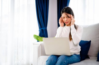 Ofis sendromu. Çok çalışan yorgun Asyalı kadın baş ağrısı çekiyor, bilgisayardan sonra görme sorunu yaşıyor. Evde yorgunluk çeken stresli genç bir kadın.