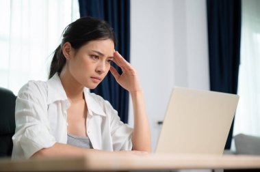 Ofis sendromu. Çok çalışan yorgun Asyalı kadın baş ağrısı çekiyor, bilgisayardan sonra görme sorunu yaşıyor. Evde yorgunluk çeken stresli genç bir kadın.