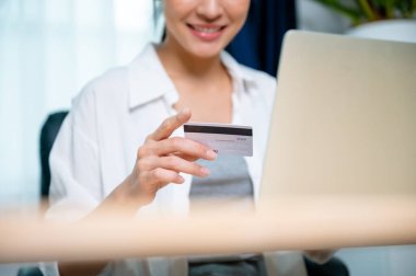 İş yerinde çalışan Asyalı genç bir kadın, internet üzerinden bilgisayar laptopunda banka kartıyla online bankacılık ödemeleri yapıyor. Kredi kartıyla internet üzerinden alışveriş yapmak