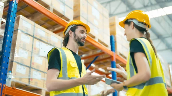 stock image Smiling workers in distribution warehouse having a cheerful conversation. They wearing vest and safety helmet in work